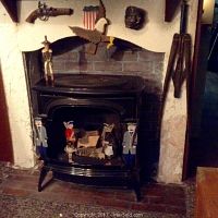 Photo of black Vermont Castings propane fireplace set in fireplace hearth with decorative figurines placed around it and various wall-mounted decor
