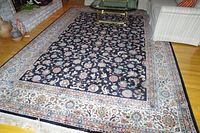 Full view of the large black Karastan rug with ornate floral designs and cream border on hardwood floor with surrounding furniture.
