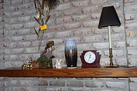 Photo of shelf showing the lamp, pottery vase, several metal and ceramic figurines, and faux succulent plants against a whitewashed brick wall.