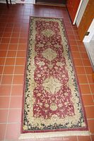 Full view of one burgundy and beige floral patterned runner rug on tiled floor
