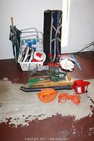 Overview photo showing Toro leaf blower, Black & Decker hedge trimmer in box, two orange extension cords, two folding lawn chairs, an umbrella, and a white basket with garden tools and supplies.