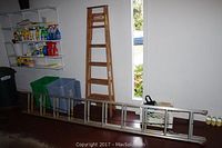 Two ladders side by side: a wooden A-frame ladder standing against the wall and a long metal extension ladder laid on the floor