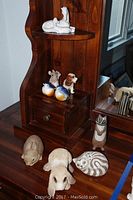 Overall view of eleven figurines on a dark wood corner shelf, showing various animals including ducks, dogs, rabbit, cat, and raccoon.