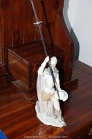 Full view of the Lladro porcelain figurine positioned next to wooden furniture, showing the man kneeling with a lance raised vertically.