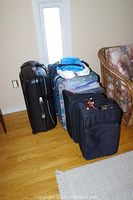 Four luggage pieces grouped near a wall and window on hardwood floor, showing varying sizes and colors including black and floral patterns.