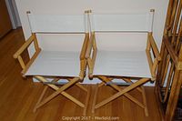 Two matching wooden director's chairs with white canvas seats and backs, sitting on a hardwood floor.