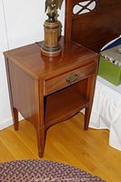 Front and side view of Heritage by Henredon nightstand with lamp on top showing drawer with brass pull and open shelf below