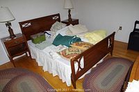Full view of full size wooden bed frame with headboard and footboard, set with pillows, blankets, nightstands and lamps in a bedroom.