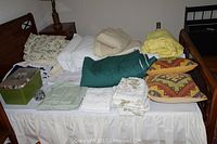 Photo showing bedding items including folded sheets, comforters, blankets, and pillows with patterned cases arranged on a bed.