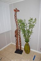 Photo showing the large giraffe statue standing next to the metal vase with faux bamboo in a corner of a room.