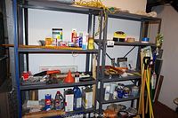 Photo of two large metal shelving units filled with various hardware, paint cans, tools, and gardening items.