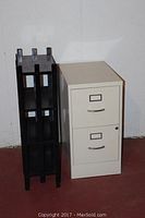Photo showing metal file cabinet and black wooden shelf side by side on red floor against white wall.