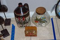 Three hand painted Pennsylvania Dutch decor items. Ceramic jug, glass jar with wooden lid, wooden napkin holder. Each with traditional floral folk art by EMS, Spanniger.