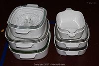 Stacked white ceramic casserole dishes with clear glass lids of various sizes.
