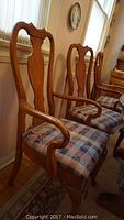 Front view of two oak captain's chairs with upholstered seats and carved curved wooden backs and armrests.