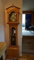 Full view of the grandmother clock showing the pine case, glass panels, pendulum, and clock face.