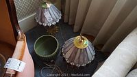 Two stained glass shade brass lamps placed on floor next to ceramic planter, cords visible, lampshades showing colors of pink, white, and burgundy