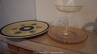 Photo of a 12 inch footed porcelain plate from France with painted leaf and fruit patterns beside a tall clear glass tiered plate with stem.
