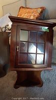 Photo showing one of the corner cabinets with glass door, brass handle, dark wood finish and a curved shelf below the door.
