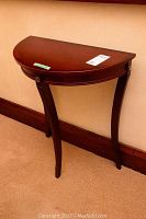 Wooden half moon table with polished dark brown finish and curved legs shown against wall.