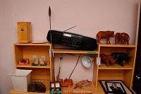 Wide view of bookcase shelves showing various items including wooden animal sculptures (water buffalo, elephant, two rhinos), stereo system, framed picture, wooden toy truck, two sets of stone bookends, and task light.