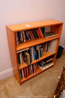 Full view of the wooden bookcase filled with books organized on three shelves.