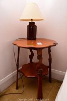 Full view of vintage round oak side table with bottom shelf and ceramic lamp