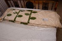 Folded queen size quilt with beige and green leaf pattern and tag visible.