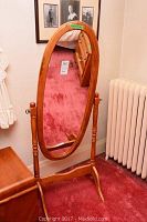 Full view of the oval oak wood floor mirror on stand showing its height and supporting base with surrounding room context.