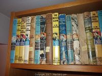 Shelf with vintage Hardy Boys books by Franklin W. Dixon, showing original dust jackets in worn condition, various titles visible.