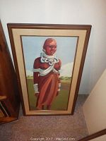 Full view of one of the paintings showing a standing figure in rust-colored traditional attire with white adornments, framed and leaning against wall.