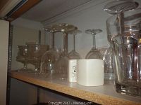 Shelved collection of assorted clear glassware including stemmed glasses and small containers.