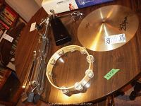 Table with cymbal stand folded, white frame tambourine, black cowbell, and Zildjian cymbal