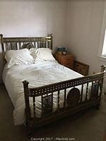 Full assembled brass bed frame with white bedding and pillows, side nightstand and artwork