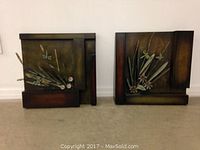Pair of square metal art pieces displayed on the floor with dragonfly and floral raised metal designs on a dark patina background.