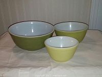 Set of three vintage Pyrex nesting bowls arranged side by side, showing exterior colors from pale yellow small bowl to olive green larger bowls