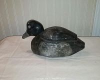 Side profile view of the hand carved dark wooden duck decoy with glass eyes showing wear and aging.