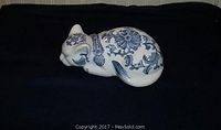 Side view of the sleeping cat figurine showing floral patterns on the body and face, placed on a dark surface for contrast.
