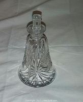 Clear pinwheel crystal perfume bottle with starburst cut pattern and faceted stopper, sitting on white fabric background.