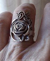 Close-up photo of the ring worn on a finger showing the detailed rose, leaves, and vines design in sterling silver.