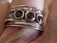 Front view of sterling silver wide band ring with three bezel set round garnet stones on top worn on finger.