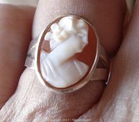 Close-up of the ring worn on finger showing white cameo profile of a lady in oval bezel with reddish background.
