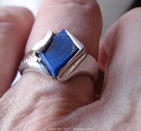 Close-up photo of the ring worn on a finger showing the diamond-shaped blue lapis lazuli stone with gold flecks and sterling silver band.