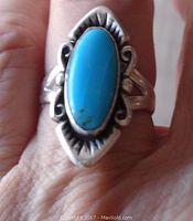 Front view of vintage Navajo sterling silver ring with long oval turquoise stone worn on finger.