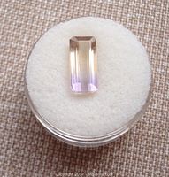 Top view of the octagonal emerald-cut natural ametrine gemstone on white padding, showing color gradient from yellow to purple.
