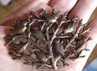 Top side of the brooch showing the design of eight birds on branching twigs with bronze tone finish.