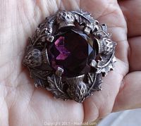 Front view showing the faceted deep purple glass center stone with pewter finish leaves and thistles.