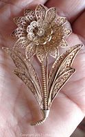 Close-up photo of the front of the vintage filigree flower brooch showing intricate openwork silver petals and two leaves with detailed patterns. The brooch is held in hand for scale.