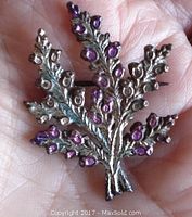 Front side close-up of vintage metal thistle pin with pink and lavender accents on leaves and buds held in hand to show size and detail.