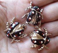 Set of three silver-tone ladybug pins with black enamel wings spotted in red and white, and green rhinestone eyes, held in a hand showing front details.